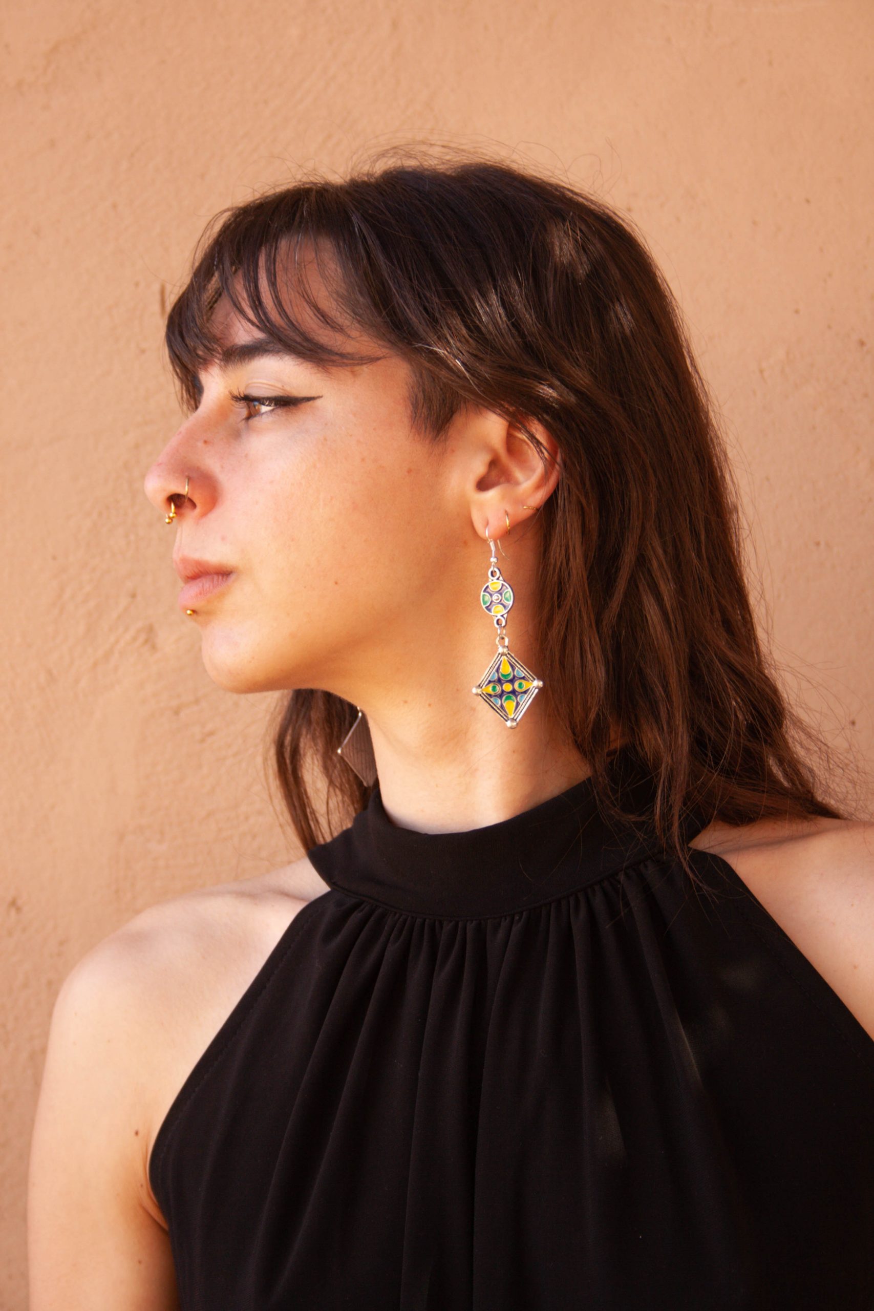 Juliette aka créatrice d'Atelier Reinette, une jeune femme brune avec frange et piercing portent des longues d'oreilles pendantes en émail