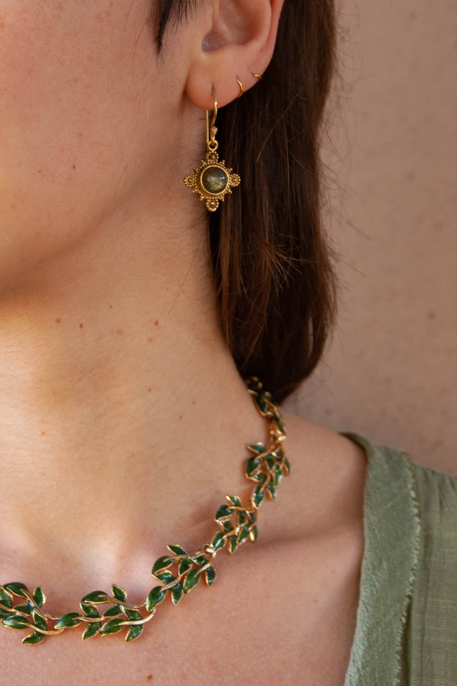 Boucle d'oreille indienne en laiton doré et labradorite portée avec un collier représentant des feuilles verte faite en émail dans des tons chauds